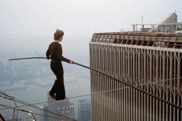 A tightrope walker balancing on a wire high above a city, beside a skyscraper